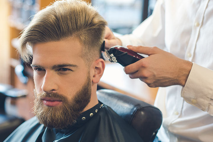 najmodniejsze męskie fryzury, mężczyzna siedzący w salonie barberskim podczas strzyżenia